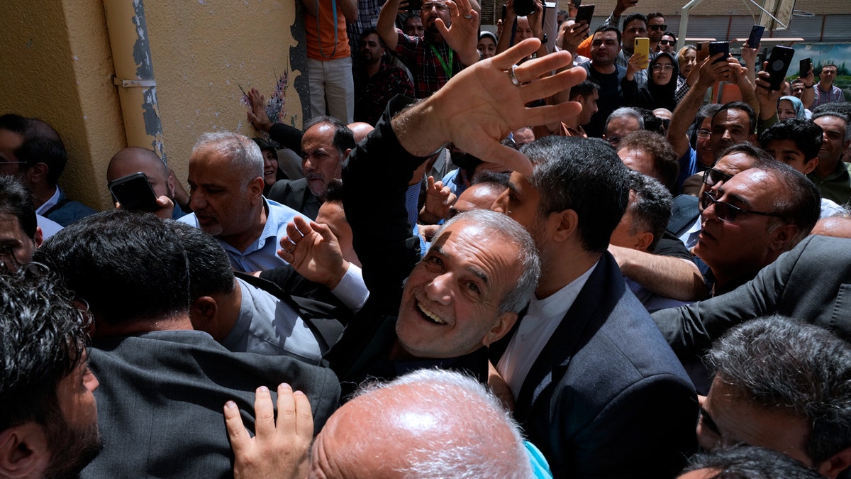 Reformist candidate for the Iran's presidential election Masoud Pezeshkian waves to the camera in the middle of a crowd while arriving to vote.