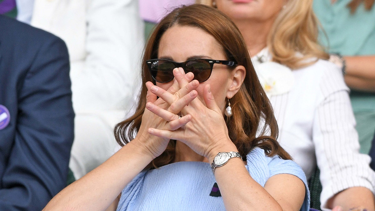 Kate Middleton in a blue dress puts her hands over her mouth watching Wimbledon