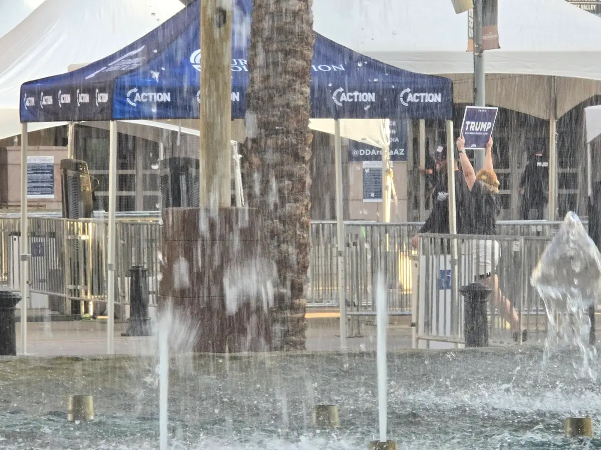 A woman carrying a Trump sign walks past a water fountain in Glendale, Ariz., on Aug. 23, 2024. (Allan Stein/The Epoch Times)