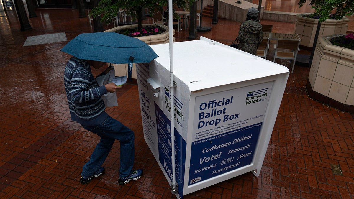 Person with umbrella puts ballot in box in Portland