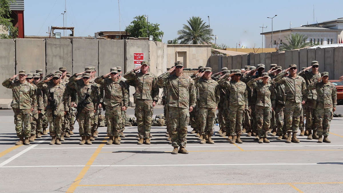 Service members supporting Operation Inherent Resolve stand in formation and salute the United States flag during a Memorial Day ceremony at Union III in Baghdad, Iraq, on May 27, 2024.