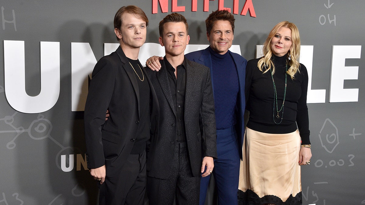 Matthew Lowe in a black suit stands next to John Owen Lowe in a black suit next to father Rob Lowe in a blue shirt and fitted suit next to wife Sheryl in a black top and khaki colored skirt on the red carpet for 