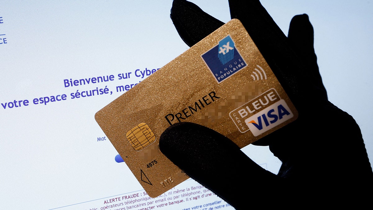 A picture shows a person holding a Visa Premier credit card in front of a computer screen displaying an internet website which bears a warning message against fraud . 