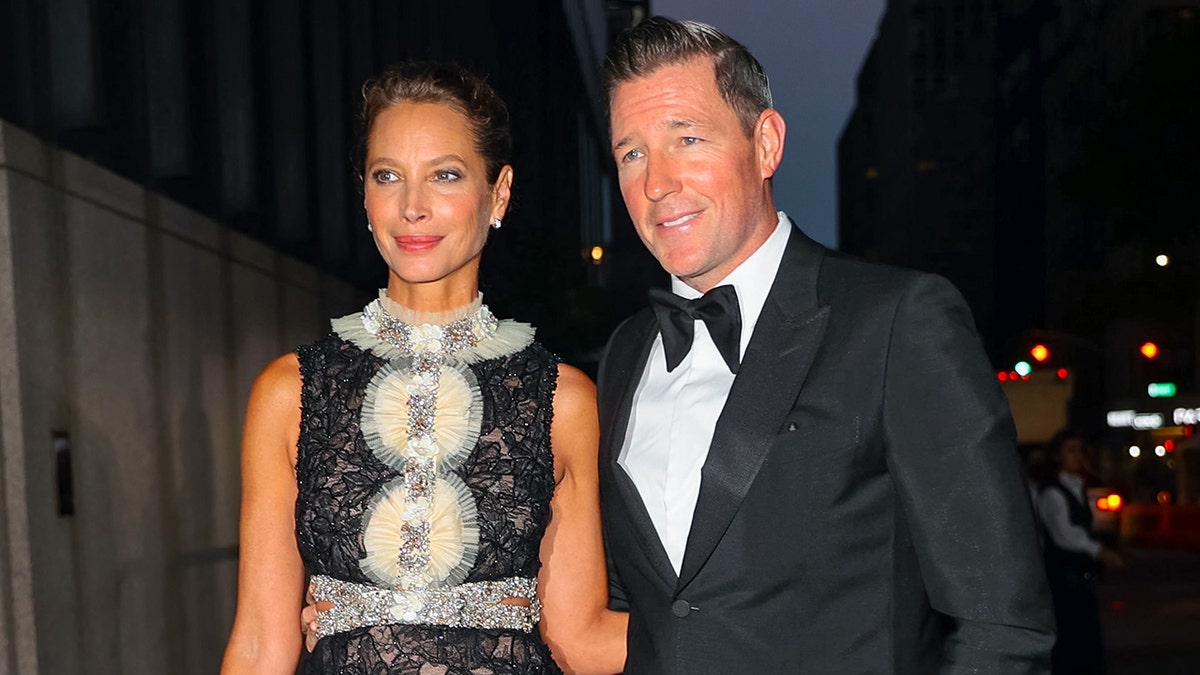 Ed Burns in a tux posing next to Christy Turlington in a black and ivory shimmering dress.