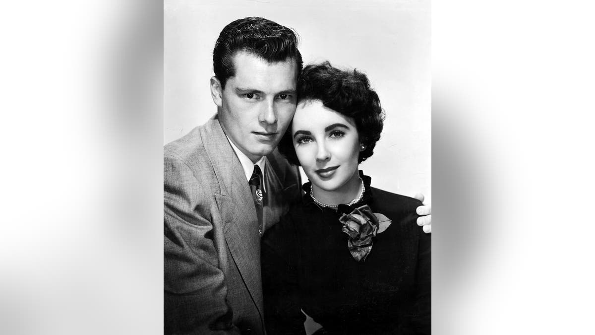 Elizabeth Taylor in a black sweater posing with her first husband, Nicky Hilton, in a suit