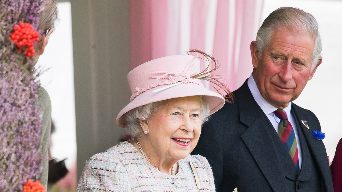 King Charles looking at his mother Queen Elizabeth II who is wearing a pink suit with a matching hat.