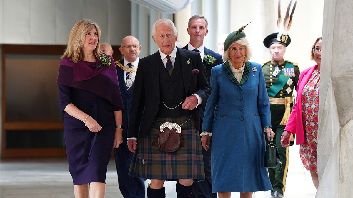 King Charles in a kilt walking with a group of people including his wife Camilla in a blue coat dress.