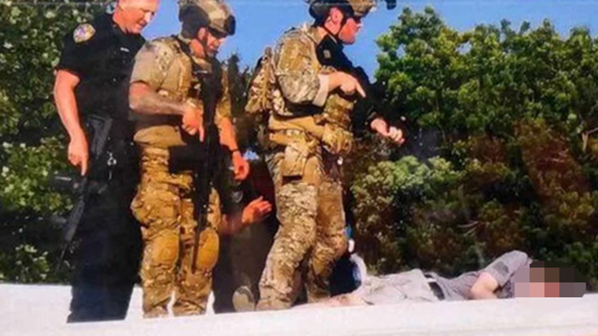 Armed men stand over a downed suspect, whose face is blurred