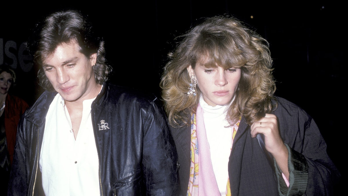 Eric and Julia Roberts both wearing black jackets walk in 1986 with their heads partially down