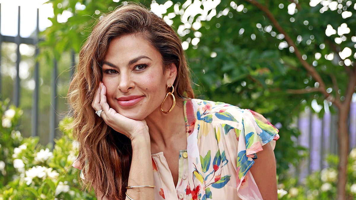 Eva Mendes soft smiles in a light pink dress with flowers as she rests her hand against her face