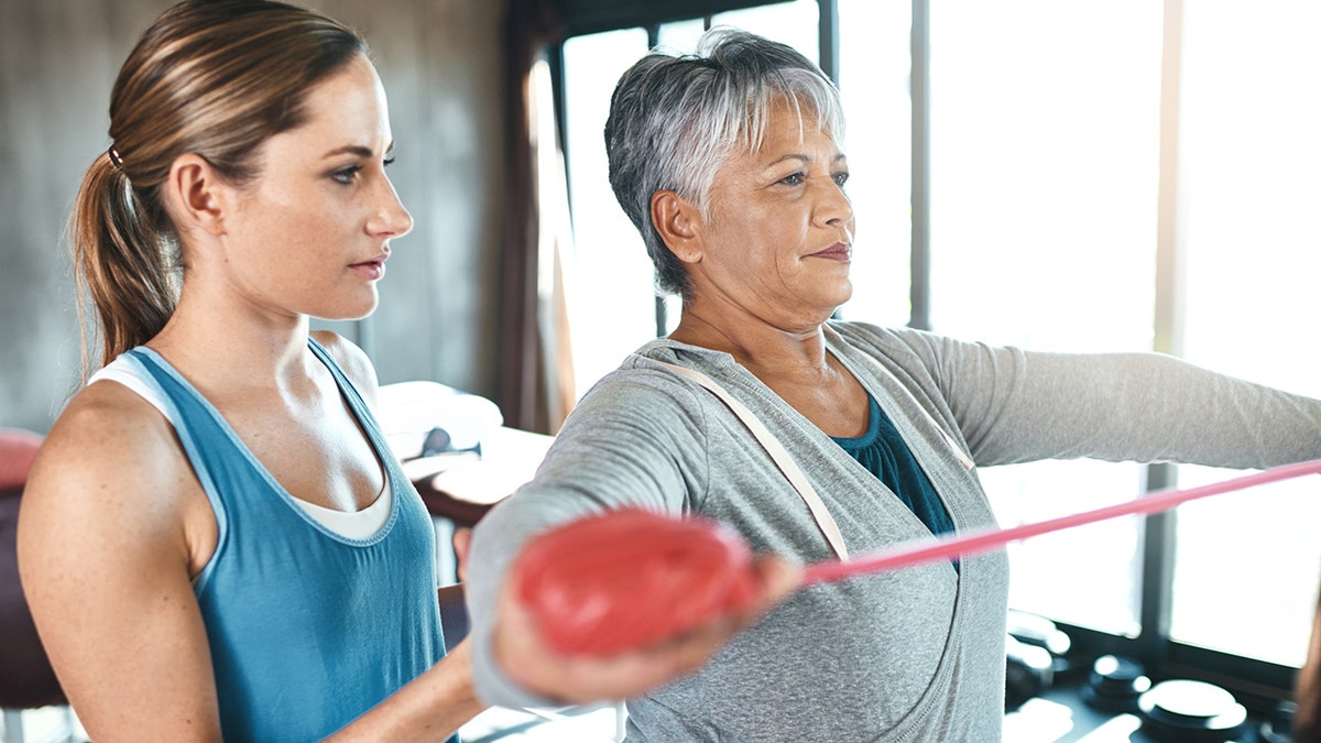 senior woman using resistance bands with the help of a physical therapist