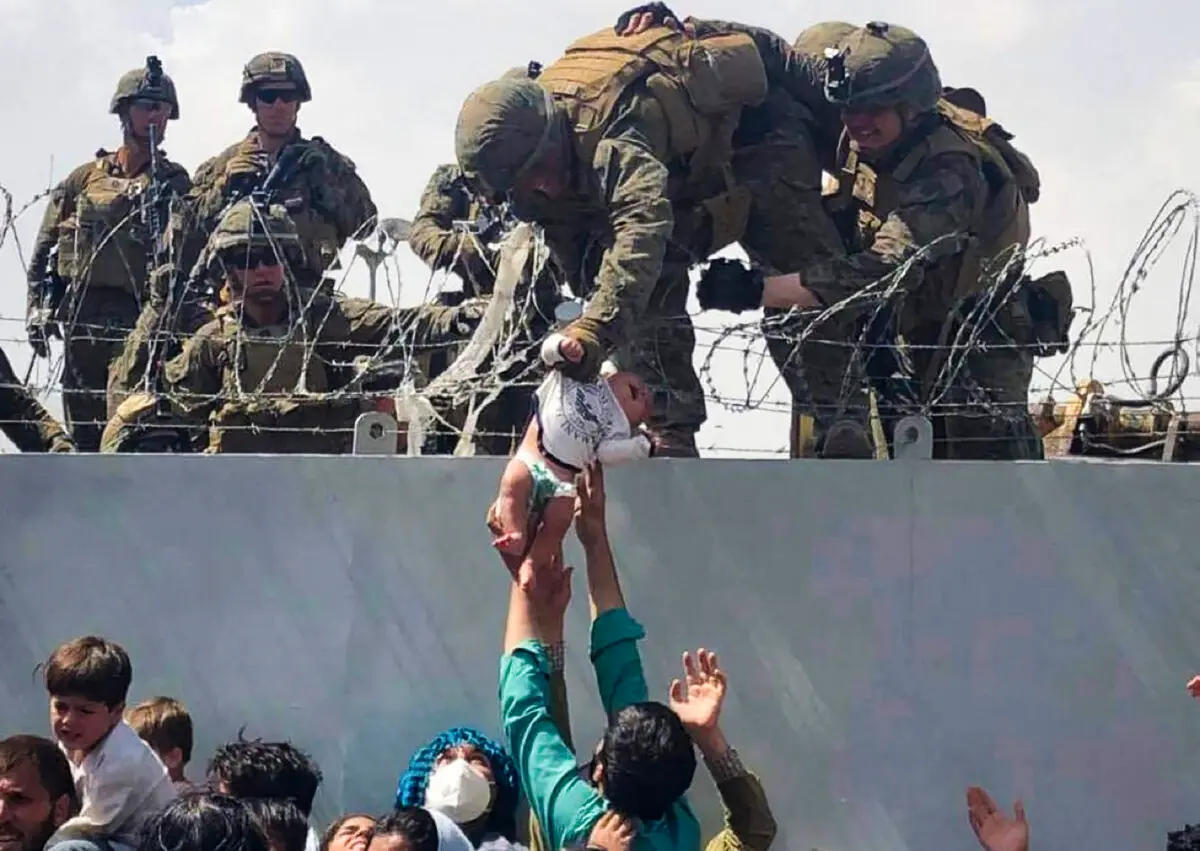 A U.S. Marine helps an infant over a barbed-wire fence during an evacuation at Hamid Karzai International Airport in Kabul, Afghanistan, on Aug. 19, 2021. (Courtesy of Omar Haidiri/AFP via Getty Images)