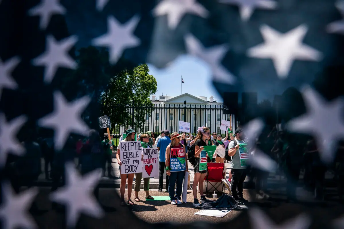 Abortion-rights activists are seen though a ripped American Flag during a rally in front of the White House in Washington, on July 4, 2022. (Nathan Howard/Getty Images)