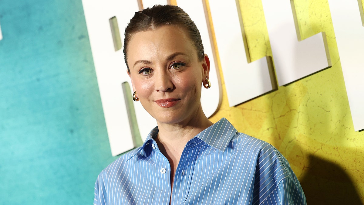 Kaley Cuoco soft smiles on the carpet wearing a blue and white striped shirt