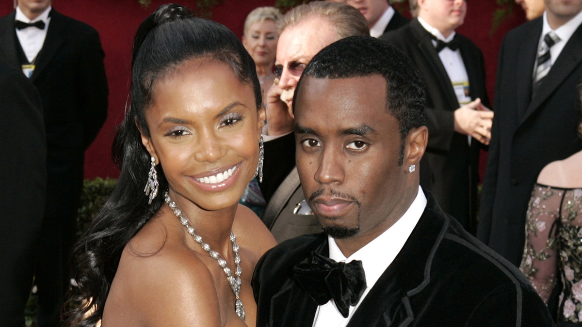 Kim Porter in orange puts her arm around Sean Combs in a grey sweater and hat