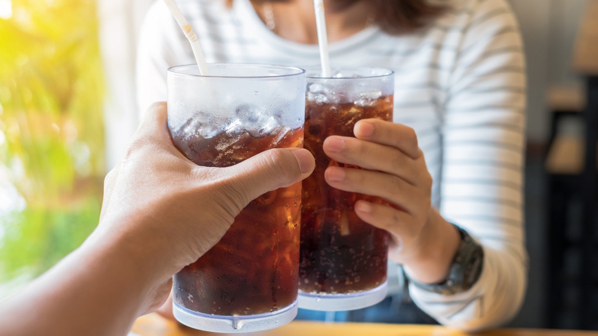 Two people clinking soda glasses