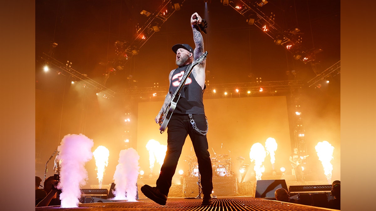 Brantley Gilbert puts his fist in the air wearing all black with fire flashing behind him on stage