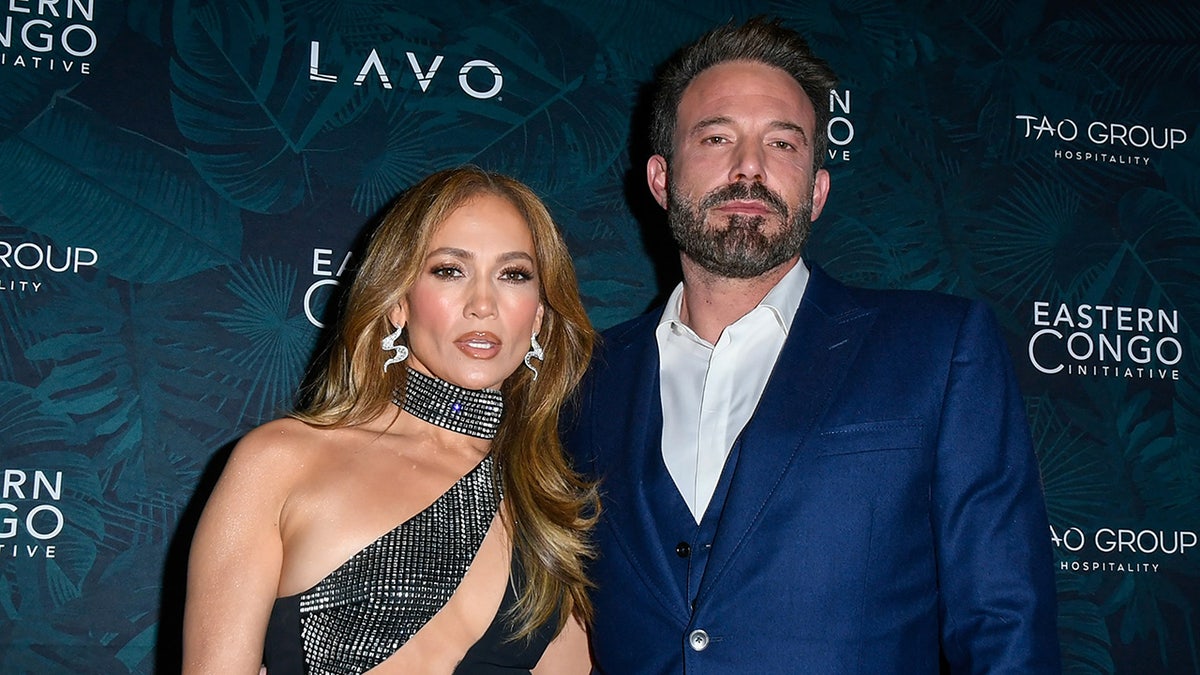 Jennifer Lopez in a cut-out dress smizes on the carpet with Ben Affleck in a blue suit