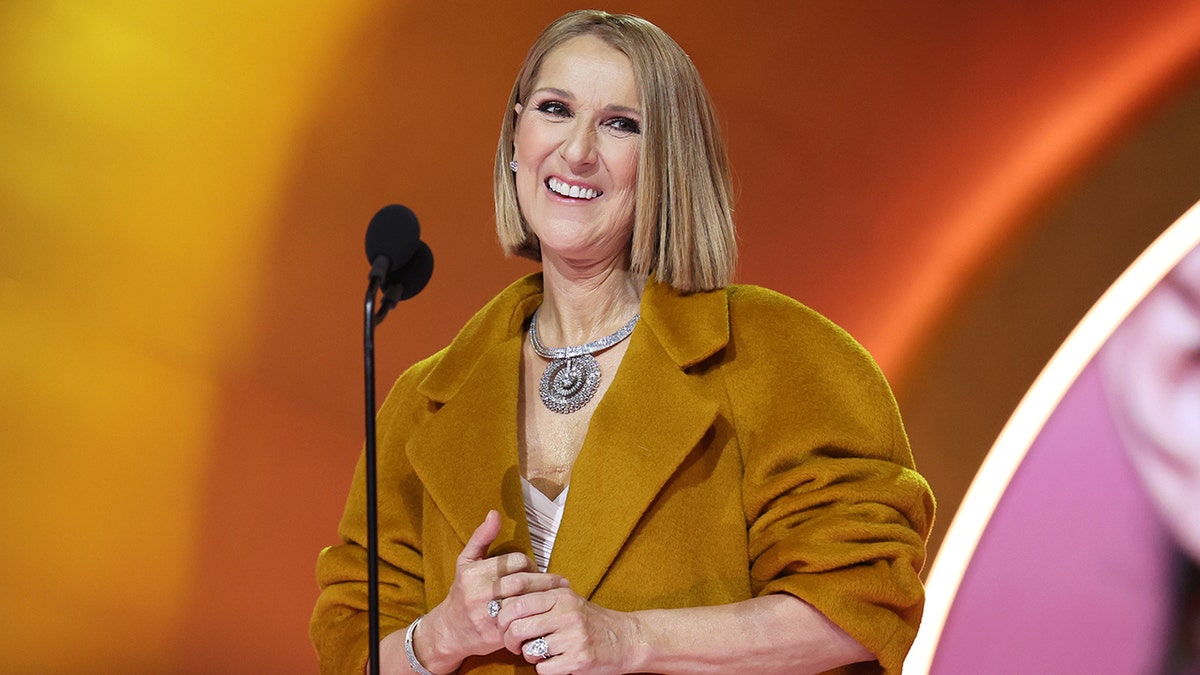 Celine Dion in a burnt orange jacket on stage at the Grammy Awards