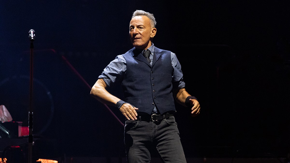 Bruce Springsteen in a blue vest and black jeans moves on stage