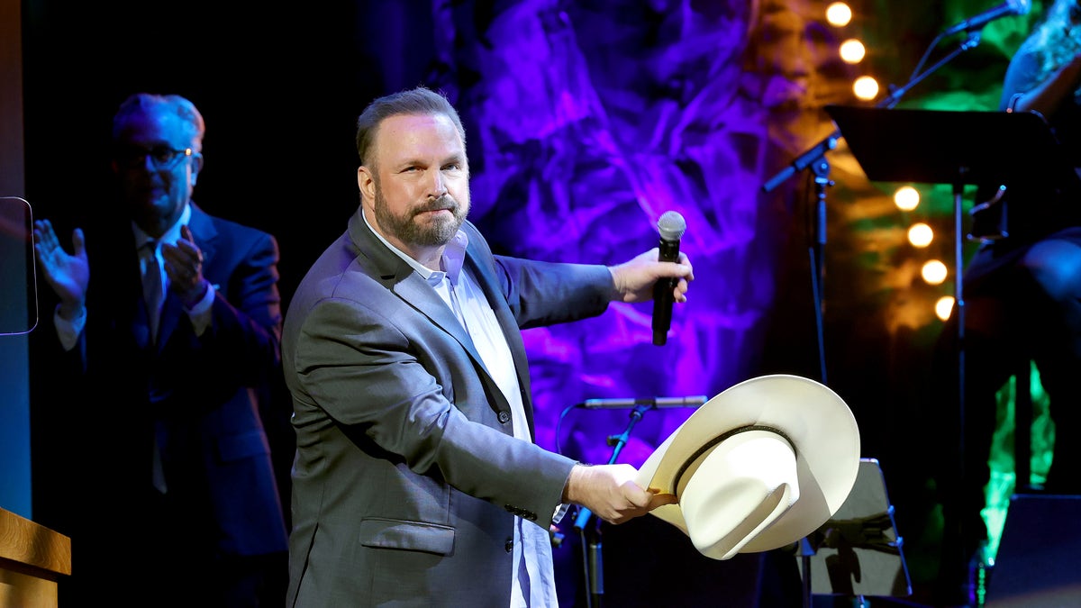 Garth Brooks performing onstage holding a microphone and his hat.