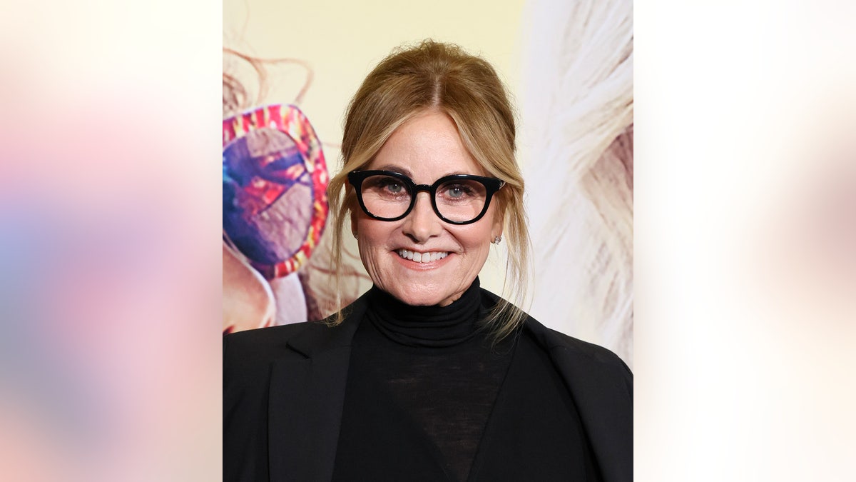 Maureen McCormick wearing a black turtleneck and matching glasses.