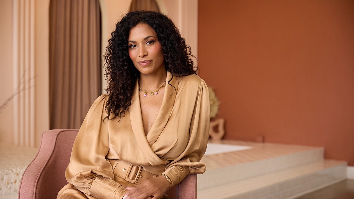 Lisa Phillips sitting in a pink chair wearing a tanned satin suit