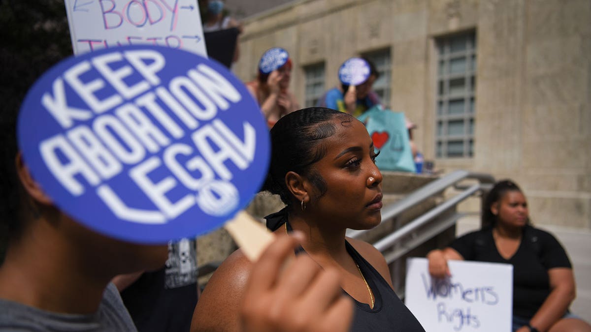 Pro-choice advocates stand outside with signs, one sign saying 