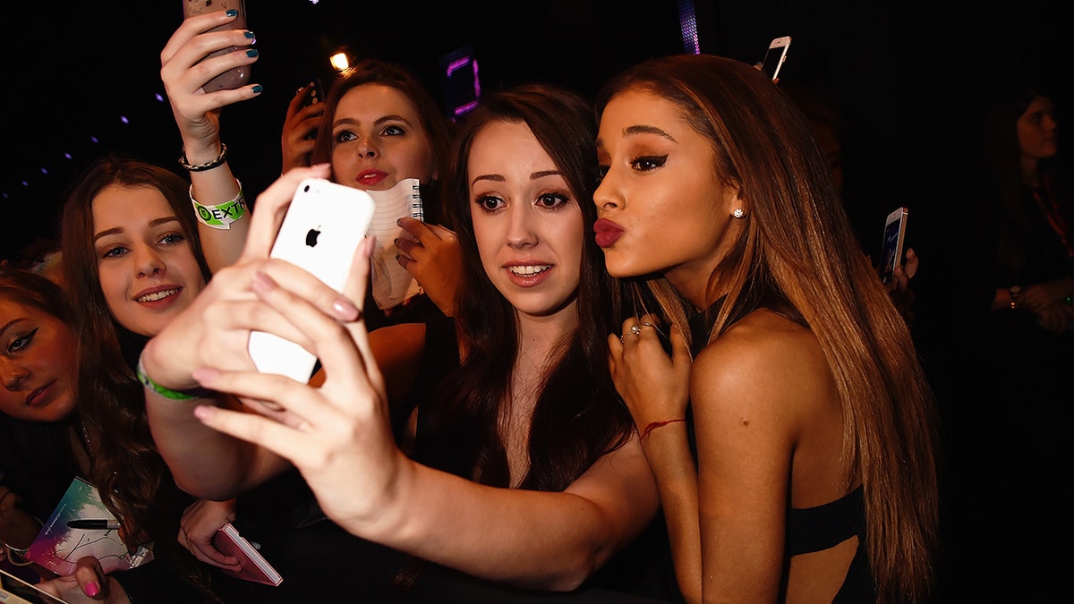 Ariana Grande makes a kissy face while taking a photo with a fan who outstreches her arms to take a selfie with her iPhone