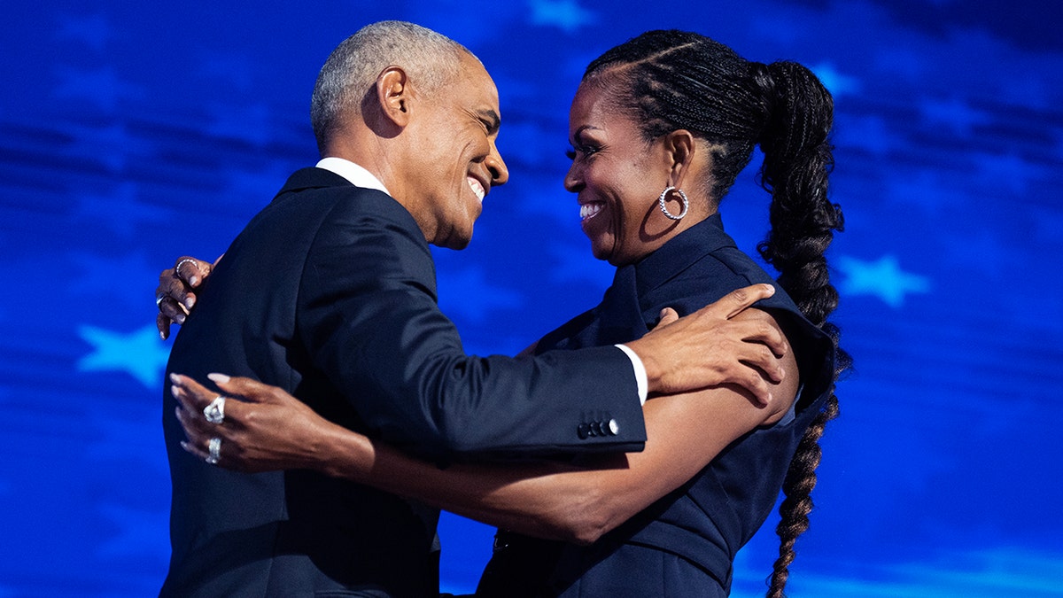 Barack Obama beams as he greets wife Michelle Obama in a navy dress on stage and they hug