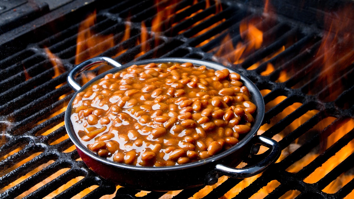 Barbecue baked beans are shown on a flaming grill.