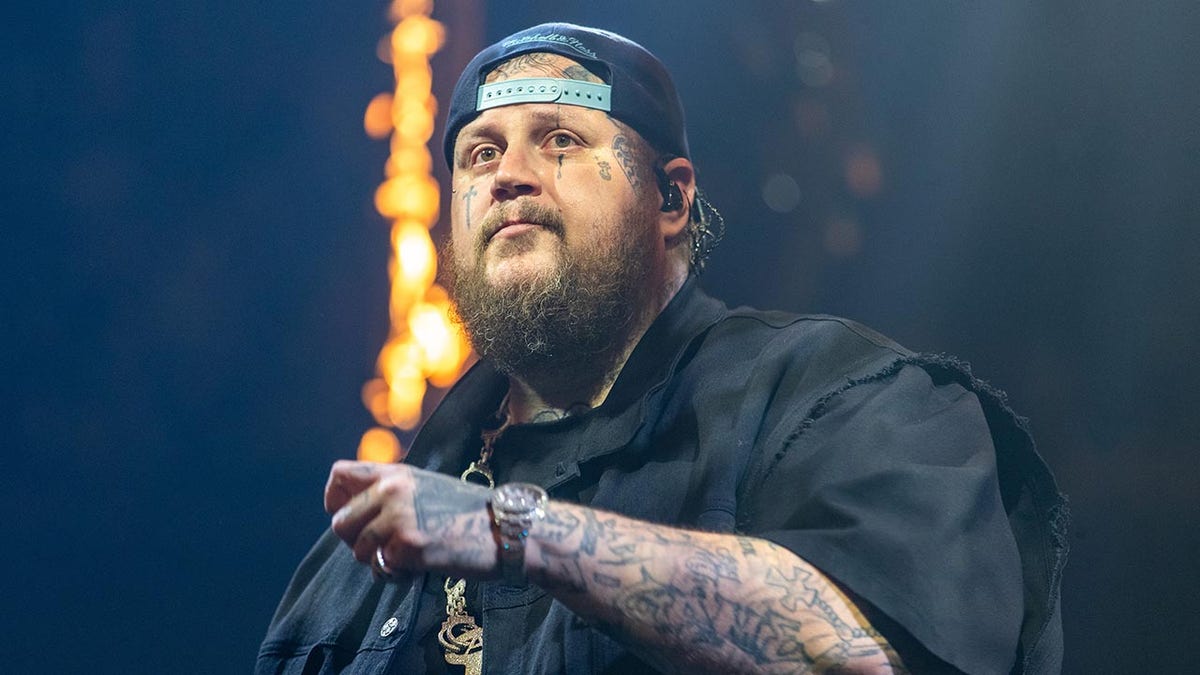 Jelly Roll in a black shirt and backward hat looks out into the distance during a performance