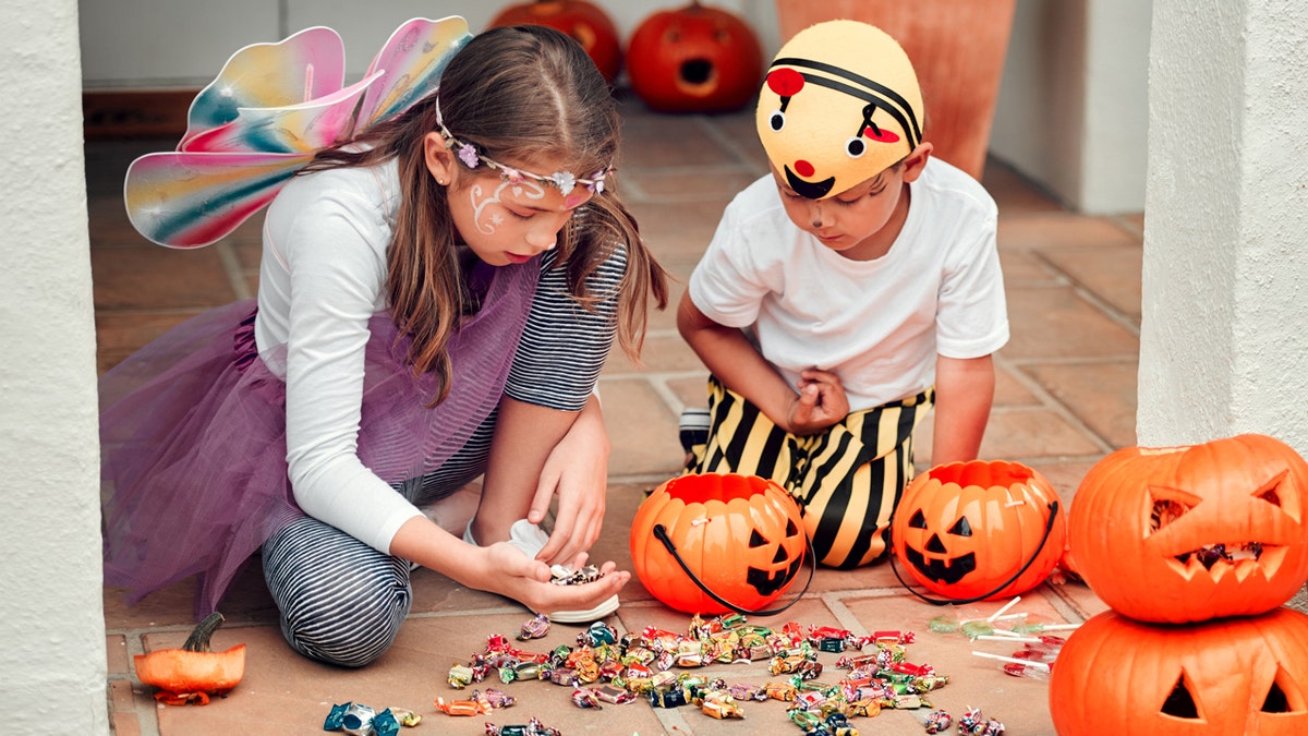 A girl and boy in costume inspect their Halloween candy.