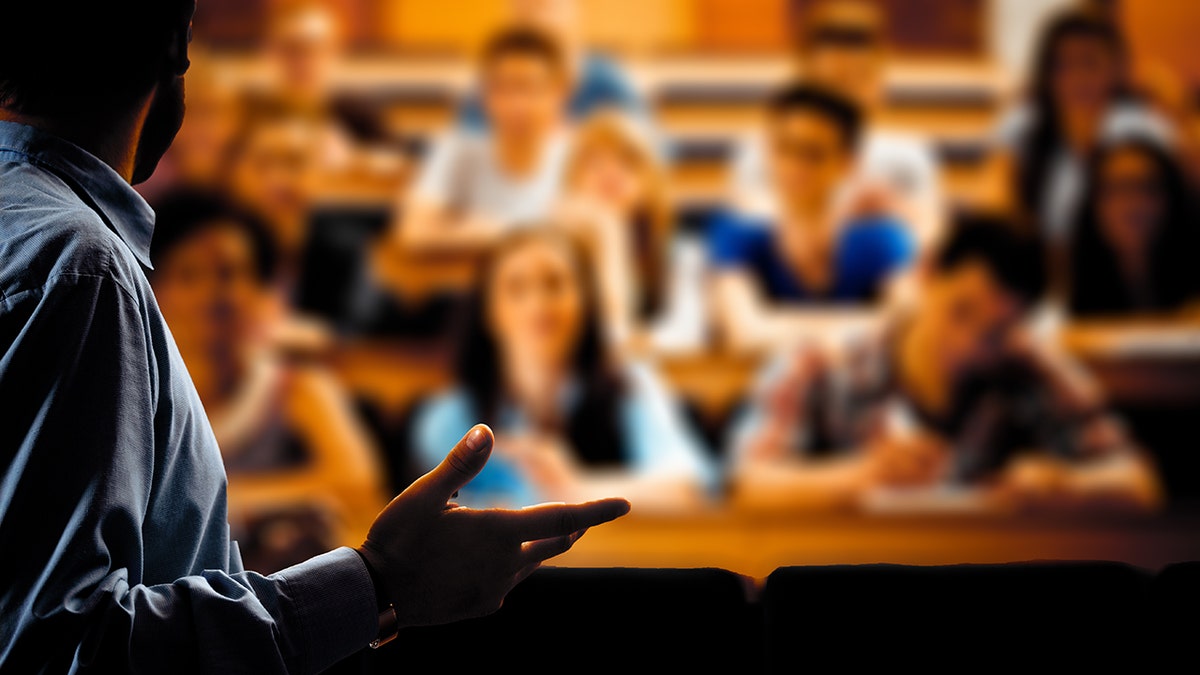 Large group of students sitting in the lecture hall at university and listening to their teacher. Focus on the professor. Dark tones.