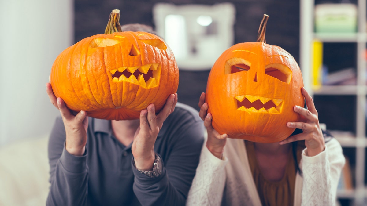 A man and woman holding carved pumpkins in front of their faces