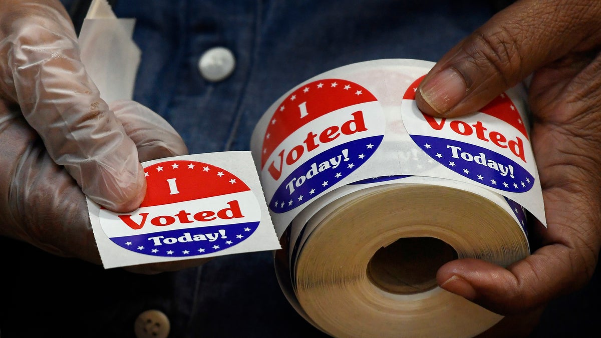 gloved hands holding a roll of I voted stickers