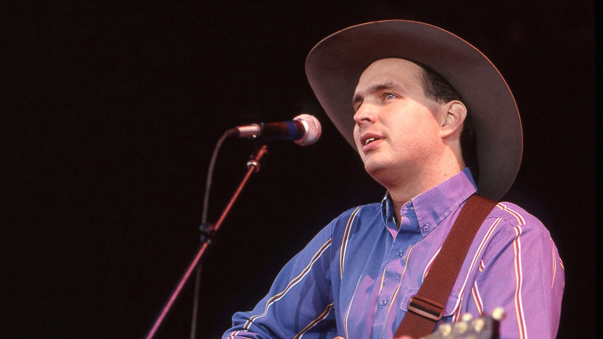 A youger Garth Brooks wears a cowboy hat and sings into a microphone