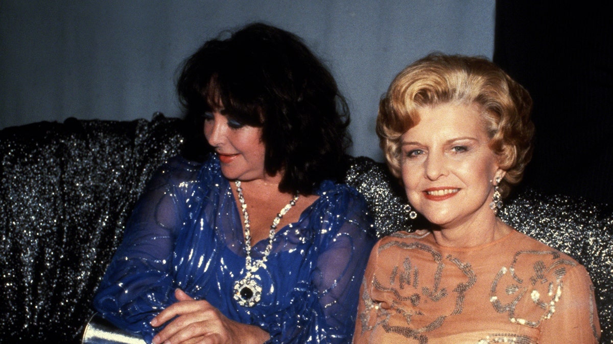 Elizabeth Taylor in a blue dress sitting next to Betty Ford in a sparkling dress.