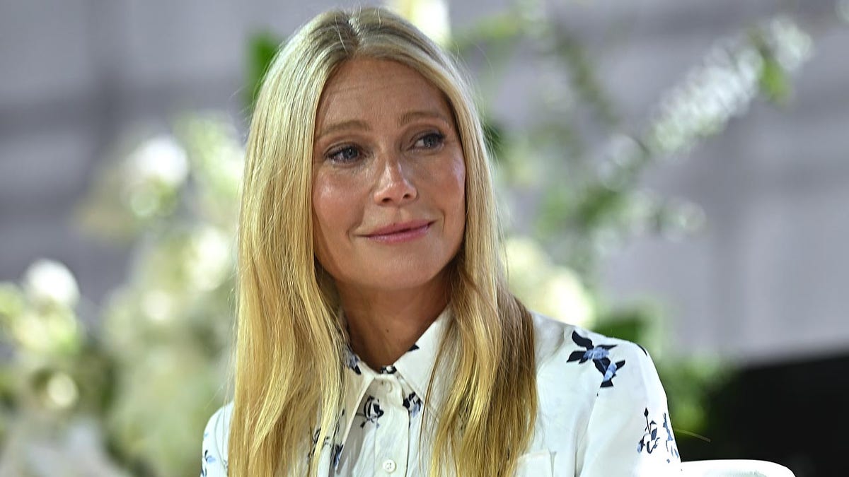 Gwyneth Paltrow in a white patterned blouse looks to her left