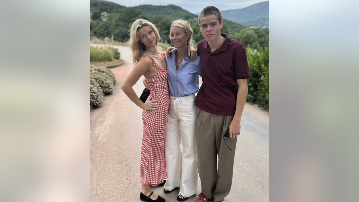 Apple Martin in a red dress poses with mother Gwyneth Paltrow in a blue top and white pants and son Moses in a red shirt and brown pants