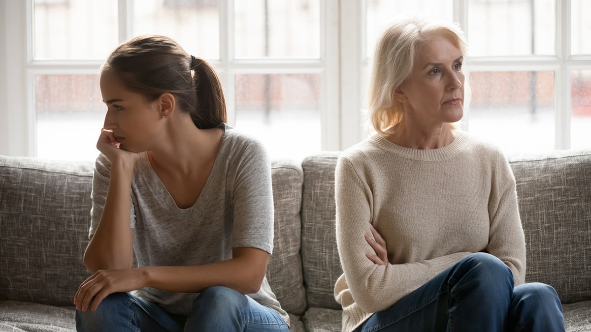 Mother and grown up daughter sit on couch separately in a fight