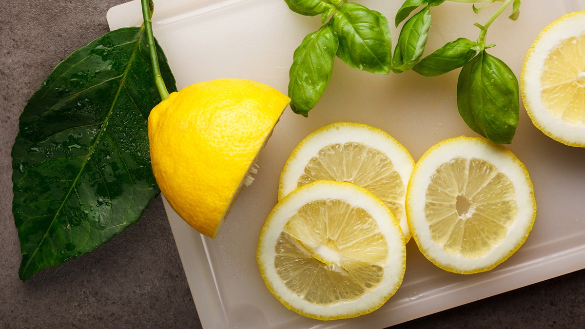 Fresh sliced lemons and basil on a cutting board.