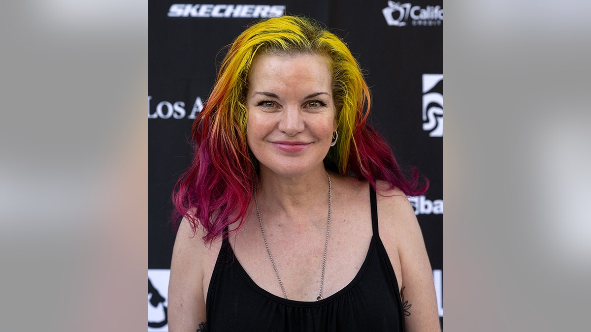 Pauley Perrette in a black top with multicolored yellow and dark pink ombré hair soft smiles on the carpet