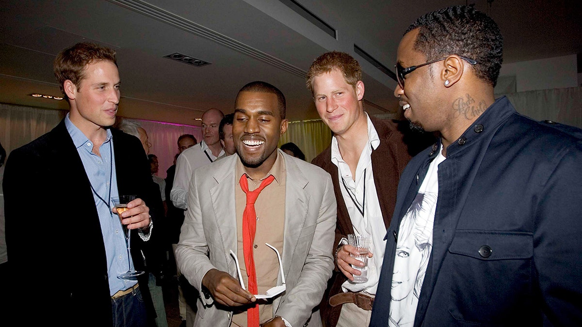 Prince William in a black jacket and blue shirt holds a drink as he socializes with a laughing Kanye West in a grey suit and red tie, Prince Harry in a brown suit and Sean 'Diddy' Combs in a navy jacket