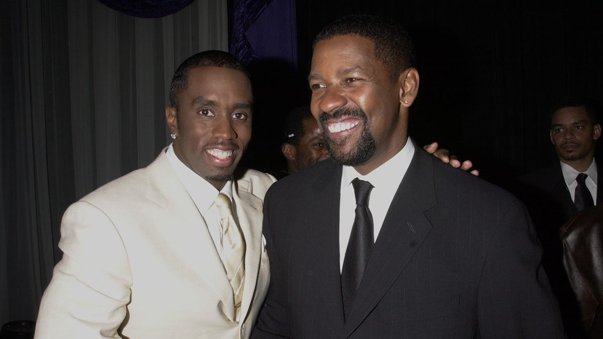 Sean Diddy Combs wears a white suit and smiles next to Denzel Washington.