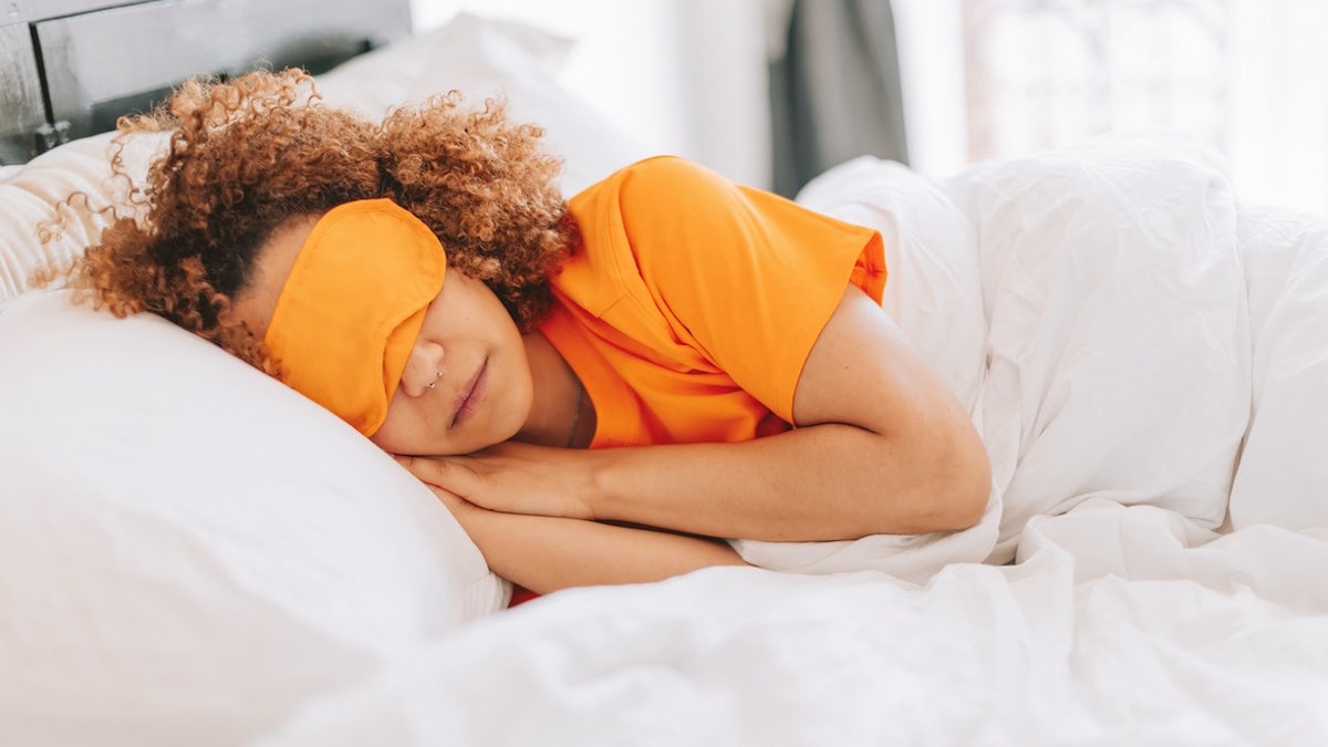 woman wearing sleep mask lying peacefully under the bed sheets