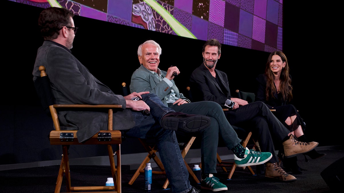 Sandra Bullock, Keanu Reeves and 'Speed' director Jan de Bont sit on stage and smile while answering questions