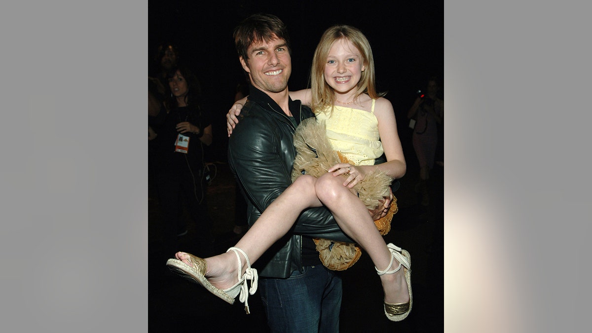 Tom Cruise in a black leather jacket holds up a grinning Dakota Fanning in a yellow dress at the 2005 MTV Movie Awards