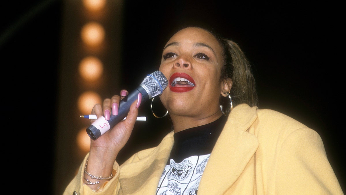 Wendy Williams holds a microphone on stage in a yellow blazer.