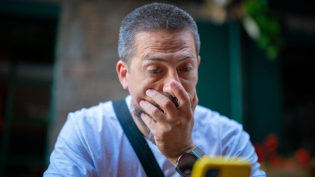 Man holds hand over mouth in shock looking at his phone